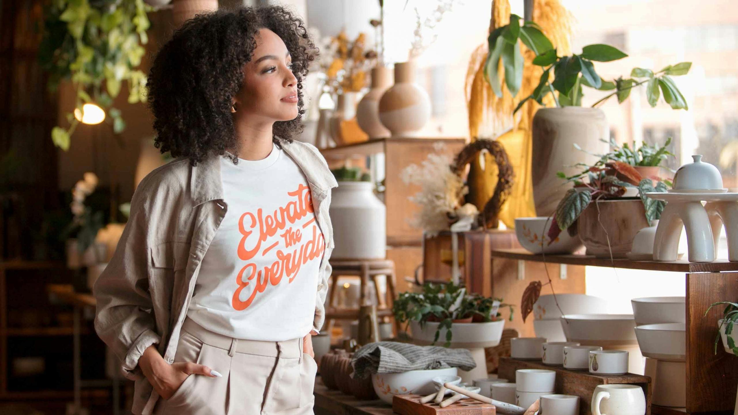 woman wearing a white shirt with elevate the everyday printed on it. 